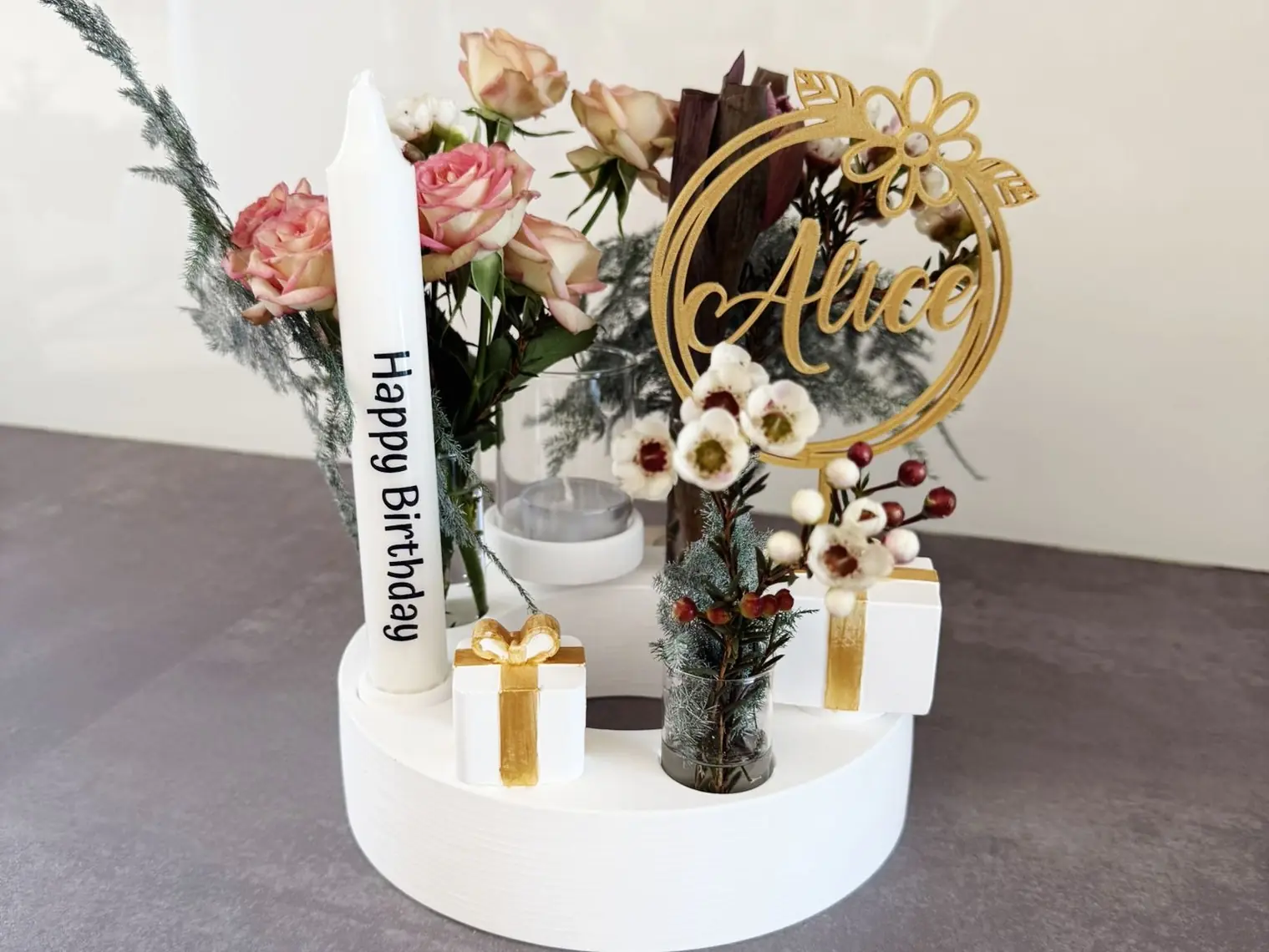 Kerzenteller mit Blumen, kleinen Geschenken und einem goldenen Namensschild
