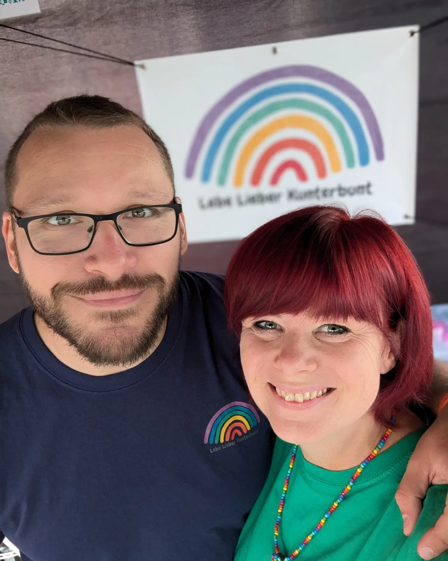 Kathrin und Marcel vor dem Banner von Lebe Lieber Kunterbunt an ihrem Marktstand
